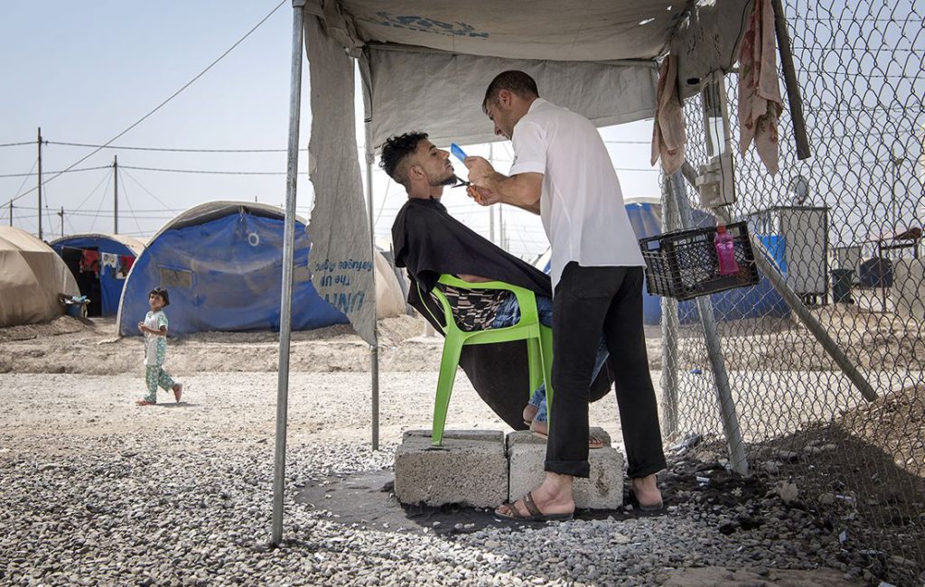 Barberaren Taher Abdelrahim klipper skägget på Haidar Mahmoud i flyktinglägret Khazer under stor koncentration. De båda männen har flytt från Mosul där de tvingades leva under IS våld under flera år. Foto: Jerker Ivarsson
